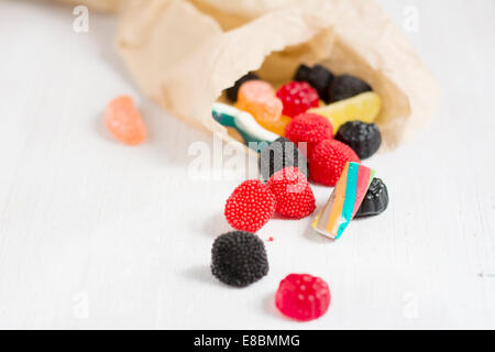 Tasche von leckeren Süßigkeiten, Gummibärchen auf weißen Tisch verstreut Stockfoto