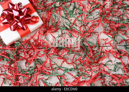 Erhöhte Ansicht eines einzelnen gewickelt Weihnachtsgeschenk in der oberen linken Ecke, umgeben von zerkleinerten roten und grünen Krepp-Papier. Stockfoto