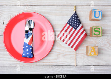 Ein Picknick-Tisch für ein 4. Juli Picknick bereit. Eine rote Platte mit Gabel und Löffel, amerikanische Flagge und Blöcke, die Rechtschreibung aus USA. Stockfoto