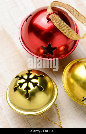 Nahaufnahme von drei Glöckchen auf einem weißen Holztisch. Zwei goldene Glocken und eine rote in Hochformat mit geringen Schärfentiefe, Stockfoto