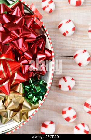 Hohen Winkel Closeup Aufnahme eine runde Dose voller Weihnachtsbänder auf einem weißen Holztisch mit roten und weißen Münzstätten verstreut. Stockfoto