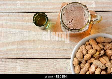 Hohen Winkel Schuss von einem Glas Bier, einem Schuss Whisky und eine Schale mit Erdnüssen auf einem weißen Holztisch. Querformat mit Kopie spac Stockfoto