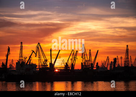 Schwarze Silhouetten von Kränen und Frachtschiffe in Varna Hafen bei Sonnenuntergang Stockfoto