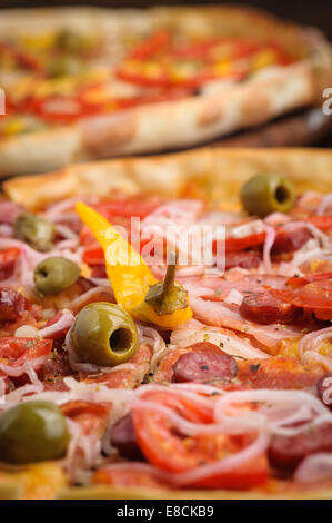 Pizza mit Salami, Peppeeoni, Oliven, Tomaten und gelbe Paprika Stockfoto