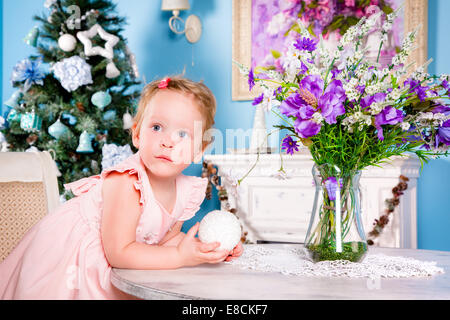 Kleines Mädchen in einem festlichen Kleid spielt in der Nähe von the Christmas tree Stockfoto