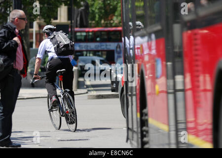 Ein Radfahrer vor einem Bus Reisen, während ein Fußgänger wartet die Straße überqueren Stockfoto