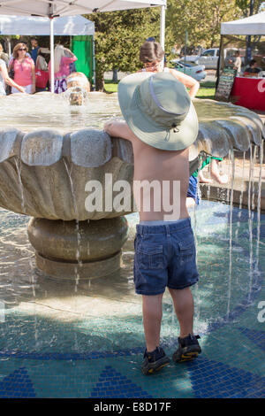 Kind spielt mit Wasser im Brunnen an einem heißen Tag in Sebastopol Bauernmarkt, Sonoma County, Kalifornien Stockfoto