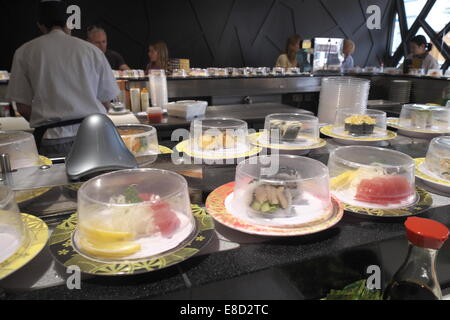japanisches Sushi-Zug-Restaurant im Norden von Sydney, Australien, Sushi-Essen auf überdachten Tellern mit Koch im Hintergrund. Stockfoto