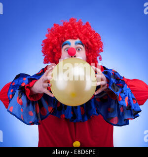 Clown im roten Kostüm mit Ballon in Händen auf blauem Hintergrund Stockfoto