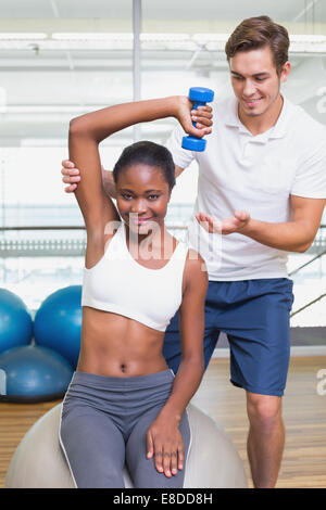 Persönliche Trainer helfen Kunden Aufzug Hantel auf Gymnastikball Stockfoto