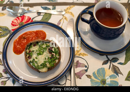 Portobello-Pilze gefüllt mit geschmolzenem Käse und frischen Kräutern, serviert mit Tomatensauce. Als Vorspeise für den Nachmittagstee. Stockfoto