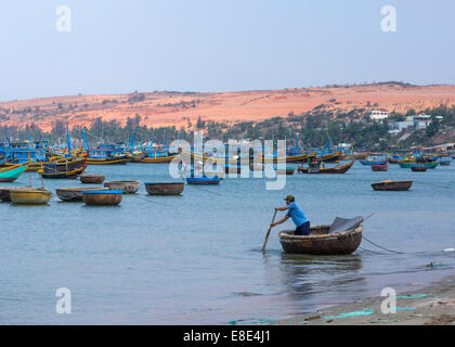 Mann Zeilen Lieferungen für die Fischereiflotte verankert vor der Küste. Stockfoto