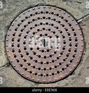 Schachtabdeckung aus Gusseisen in Steinpflaster am Hafen von Bristol UK durchbohrt Stockfoto