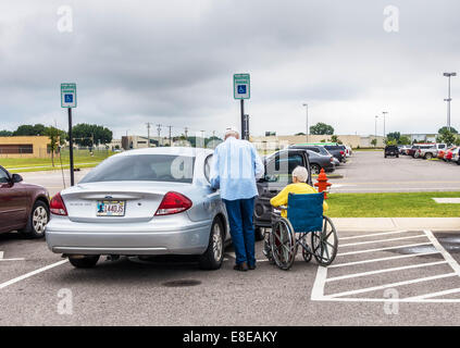 Ein älterer Mann bereitet sich auf seine behinderte Frau in ihr Auto auf einem Parkplatz in Oklahoma City, Oklahoma, USA zu helfen. Stockfoto