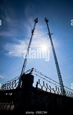 Pole mit elektrischen Drähten und Kommunikation Turm umgeben von einem Zaun Stockfoto