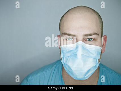 Junger Arzt mit Glatze trägt eine Maske und auf einem grauen Hintergrund (im Studio) Stockfoto