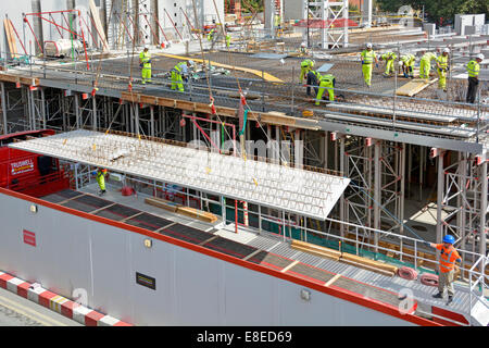 Baustellenarbeiten werden durchgeführt beschäftigte Arbeiter, Hochsichtskit und Schutzhelm über man und Kran heben Betonbodenplatte LKW Großbritannien Stockfoto