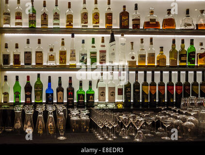 Flaschen Wein, Schnaps und Spirituosen sowie Gläser auf einem beleuchteten Bar. Stockfoto