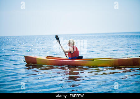 Junge Frau alleine auf einem ruhigen See Kajak und eine Warnweste tragen