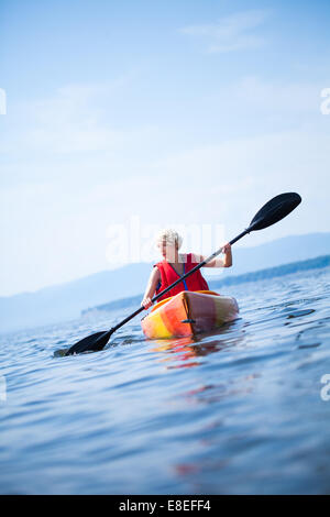 Junge Frau alleine auf einem ruhigen See Kajak und eine Warnweste tragen