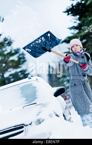 Auto-Stuck im Schnee und eine Frau, die nach einem großen Schneesturm Schaufeln Stockfoto