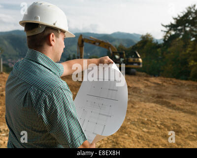 Rückansicht des männlichen Ingenieur stehend auf Baustelle lesen Blaupause Stockfoto