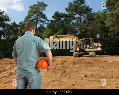 Rückansicht des Ingenieur mit Bauarbeiterhelm betrachten Bagger auf der Baustelle Stockfoto