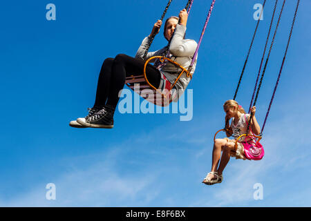 Teenager, zwei Mädchen auf dem Kettenschaukel-Karussell reiten in den blauen Himmel Stockfoto