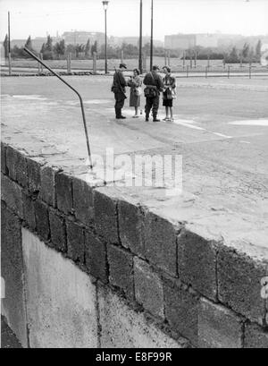 Blick über die Berliner Mauer am Potsdamer Platz (von Westen) auf zwei junge Frauen der FDJ (freie deutsche Jugend) Volks Polizist der DDR Blumen verleihen. Die Bundesrepublik Deutschland und der Deutschen Demokratischen Republik wurden durch einen Eisernen Vorhang vom 13. August 1961, der Tag der Gebäude der Berliner Mauer bis zum Fall der Mauer am 9. November 1989 in West und Ost aufgeteilt. Stockfoto