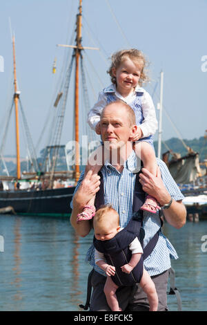 Reife Dad / Vater mit zwei / 2 Kinder; ein Kind auf Schultern und Baby im Tragetuch. Cornwall UK. Stockfoto