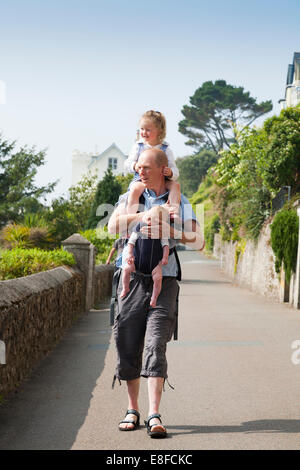 Reife Dad / Vater mit zwei / 2 Kinder; ein Kind auf Schultern und Baby im Tragetuch. Cornwall UK. Stockfoto