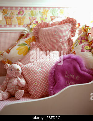 Rosa aufgegebenes Teddybär und passende Kissen auf Kinderbett mit lila flauschige Kissen Stockfoto
