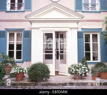 Weiße Impatiens in Töpfen auf beiden Seiten der Hälfte verglasten Türen des französischen Landhaus mit blauen Fensterläden Stockfoto