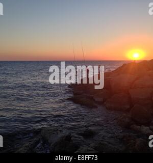 Silhouette der Fischer stehen auf Felsen Angeln bei Sonnenuntergang, Tel Aviv, Israel Stockfoto