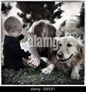 Mutter, Sohn und golden Retriever Hund auf Rasen sitzen Stockfoto