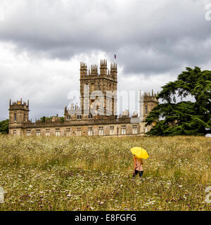 UK, Hampshire, Highclere Castle, Frau mit gelben Regenschirm auf Wiese Stockfoto