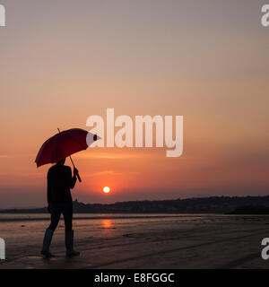 Person aufwachen mit Sonnenschirm am Strand bei Sonnenuntergang Stockfoto