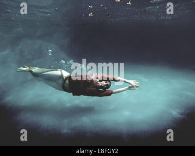 Voll bekleidete Frau mit geschlossenen Augen schwimmend unter Wasser in einem Schwimmbad Stockfoto