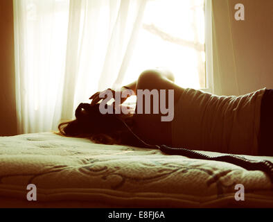 Rückansicht einer jungen Frau, die auf einem Bett liegt und Musik hört Stockfoto