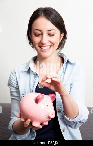 Porträt einer lächelnden jungen Frau, die eine Münze in ein Sparschwein steckt Stockfoto
