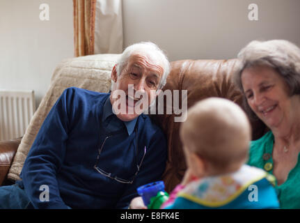 Großeltern sitzen auf einem Sofa und spielen mit ihrem Enkel Stockfoto
