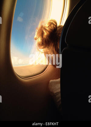 Rückansicht EINES Mädchens, das in einem Flugzeug am Fenster sitzt Stockfoto