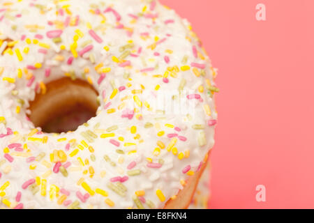 Nahaufnahme eines Donuts mit Glasur und Besprengung auf einem rosa Hintergrund Stockfoto