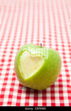 Herzform fehlt an der Seite eines grünen Apple auf einer karierten Tischdecke Stockfoto