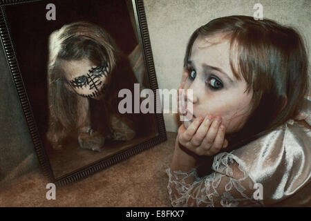 Mädchen auf dem Boden liegend mit einer Reflexion ihres Alter Ego im Spiegel Stockfoto