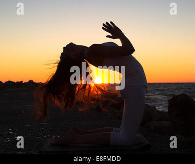 Frau praktizieren Yoga am Strand bei Sonnenuntergang Stockfoto