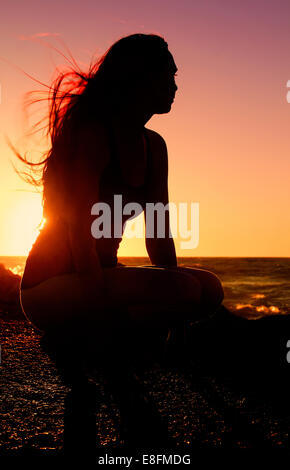Silhouette der Frau praktizieren Yoga am Strand bei Sonnenuntergang Stockfoto