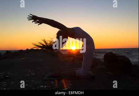 Frau praktizieren Yoga am Strand bei Sonnenuntergang Stockfoto