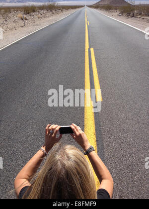 Frau, die mit dem Handy die unendliche Straße fotografiert, Nevada, USA Stockfoto