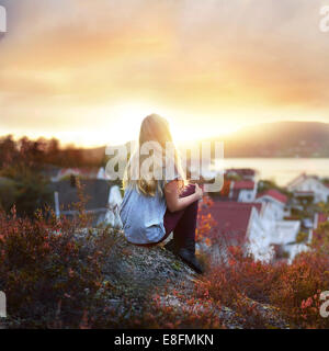 Frau sitzt auf EINEM Felsen und schaut auf die Küstenlandschaft Norwegens Stockfoto
